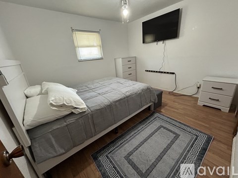 A bedroom with a bed, dresser, and a flat screen TV mounted on the wall.