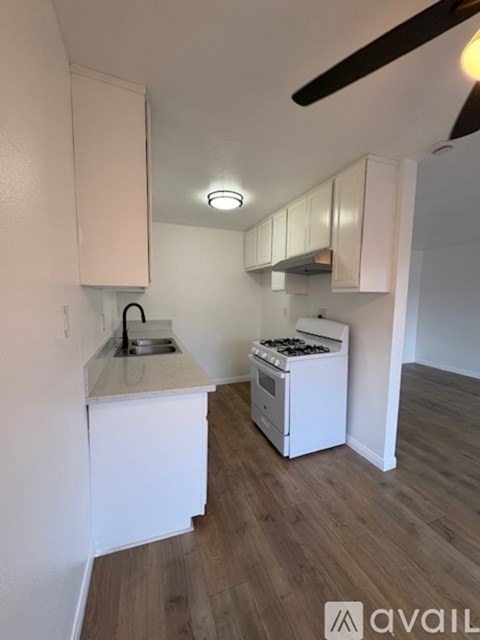 A small kitchen with white cabinets and a wooden floor.