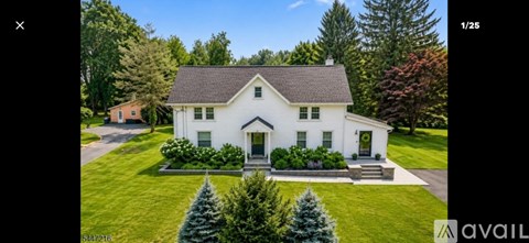 A white house with a black roof is surrounded by greenery.