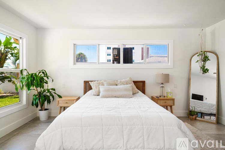 A bedroom with a large bed, a potted plant, and a mirror on the wall.