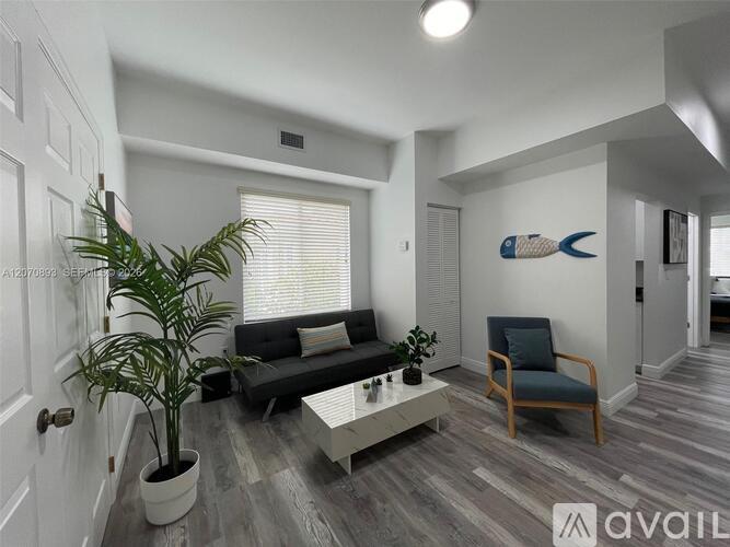A living room with a black couch, a wooden chair, a potted plant, and a painting of a fish on the wall.