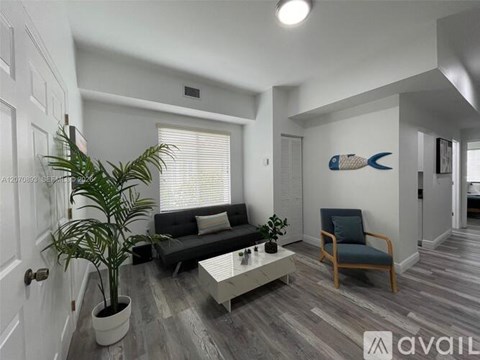 A living room with a black couch, a wooden chair, a potted plant, and a painting of a fish on the wall.
