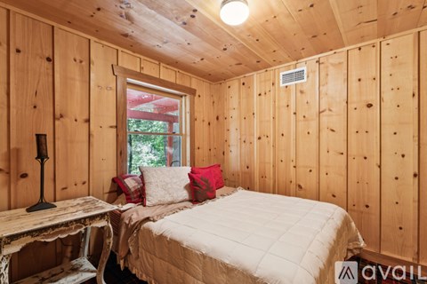 A bedroom with wooden walls and a bed with a white comforter.