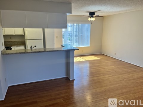 A room with wooden flooring and a kitchenette with a sink and a window.