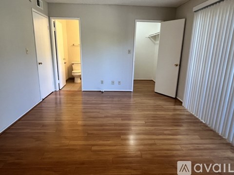 A room with wooden floors and white walls, with a toilet visible in one of the open doors.