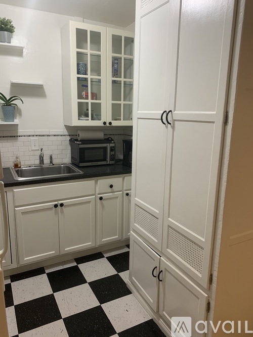 A kitchen with white cabinets and a black and white checkered floor.