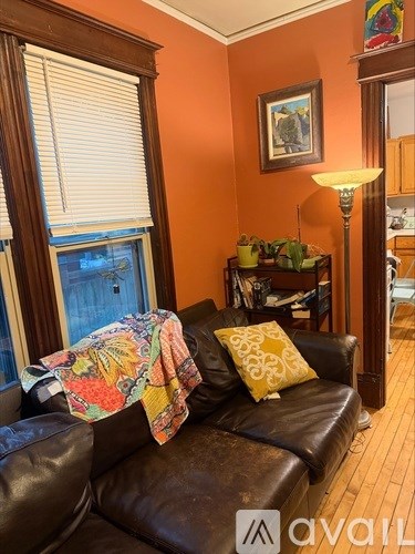 A living room with a brown leather couch and a window with blinds.