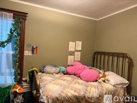 A bedroom with a bed covered in stuffed animals and a window with curtains.