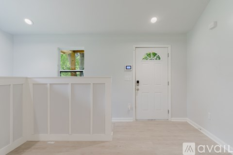 A room with a white door and a window with a view of trees.