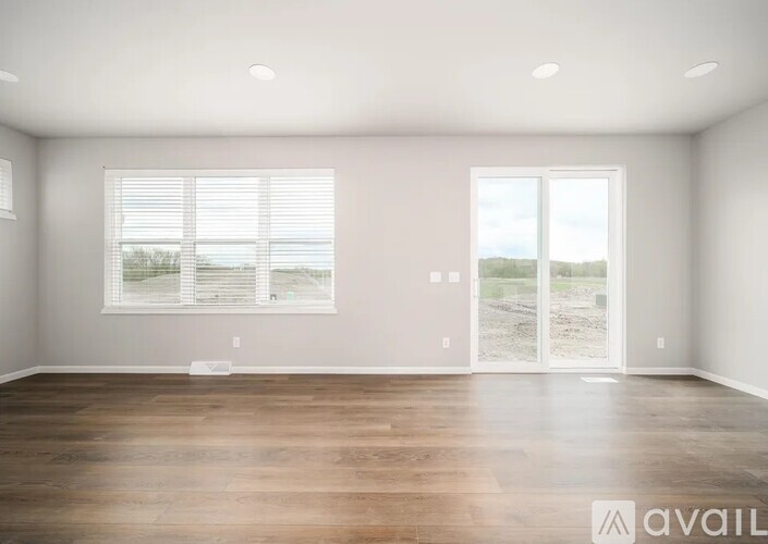 A spacious room with wooden floors and a large window with blinds.