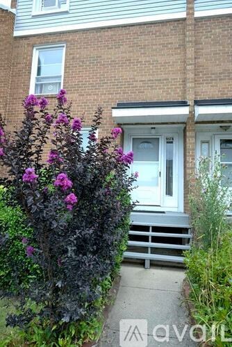 A house with a white door and windows is surrounded by greenery and flowers.