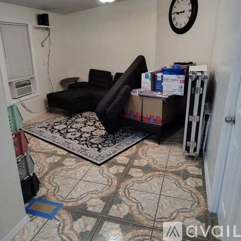 A living room with a black couch and a clock on the wall.