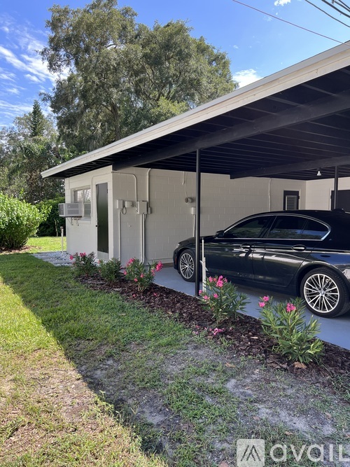 A black car is parked in front of a grey building with a white roof.