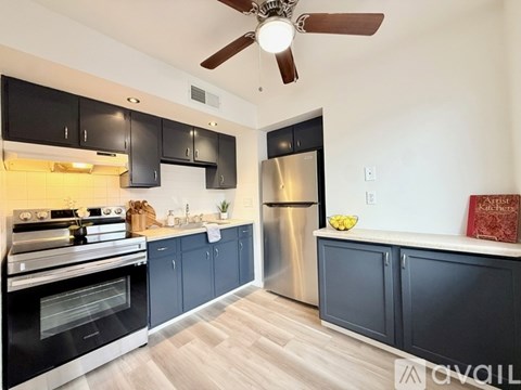 A kitchen with black cabinets and a stainless steel refrigerator.