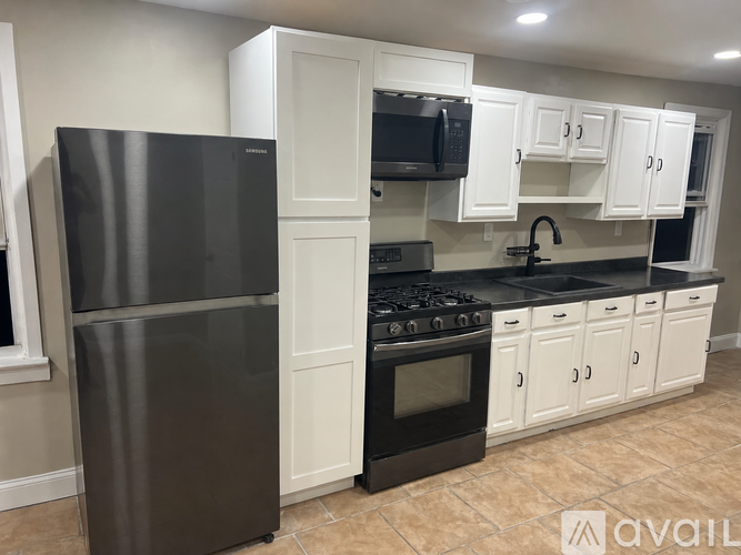 A kitchen with a black refrigerator, black stove, and white cabinets.