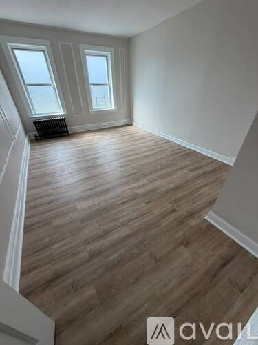A room with wooden flooring and two windows.