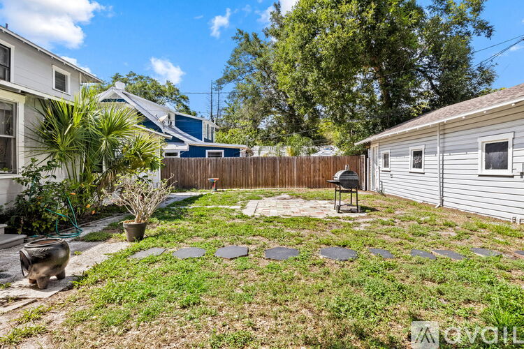 A backyard with a fence, a small tree, and a BBQ grill.