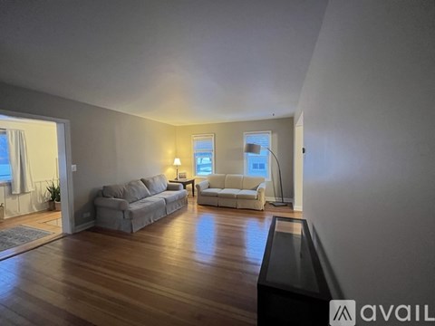 A living room with a grey couch and a white couch with a wooden floor.