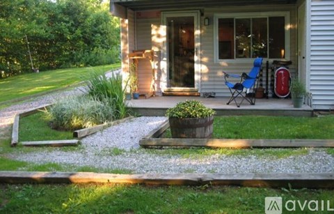 A small garden area in front of a house with a blue chair and a red object on the porch.
