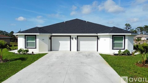 A white house with a black roof and a grey driveway.