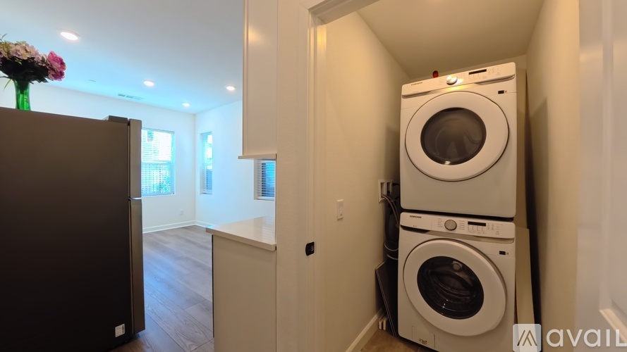 A black refrigerator is in a kitchen next to a washer and dryer stacked on top of each other.