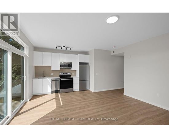 A well-lit, empty room with a kitchen area in the background.