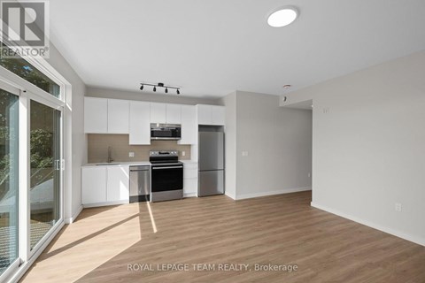 A well-lit, empty room with a kitchen area in the background.