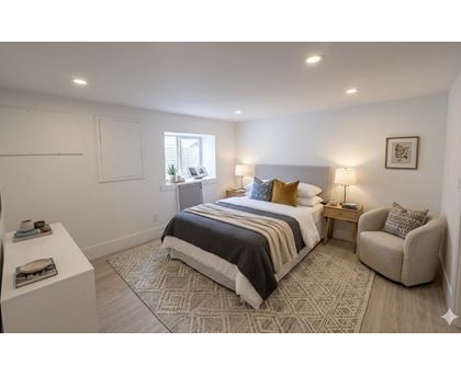 A bedroom with a large bed, a chair, and a window.