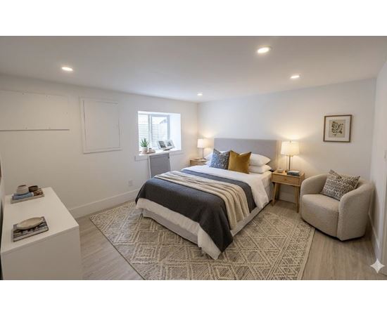 A bedroom with a large bed, a chair, and a window.