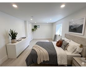 A bedroom with a large bed and a potted plant on a nightstand.