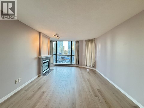 A spacious room with wooden flooring and a large window overlooking a cityscape.