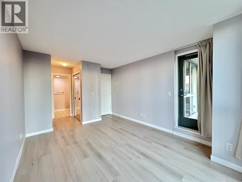 A spacious room with light wood flooring and a window with curtains.