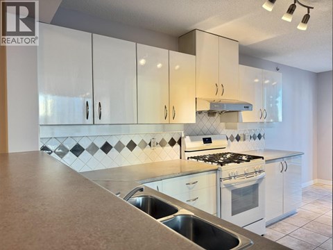 A kitchen with white cabinets and a black and white tiled backsplash.