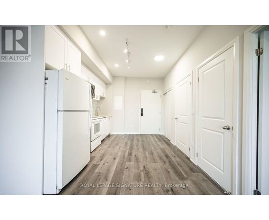 A white refrigerator is in the middle of a kitchen with wooden floors and white walls.