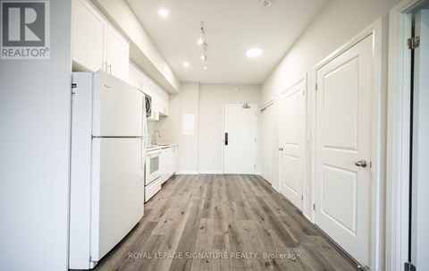 A white refrigerator is in the middle of a kitchen with wooden floors and white walls.