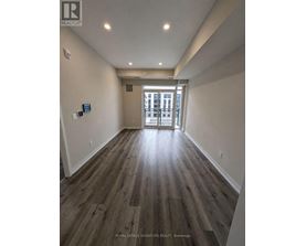 A hallway with wood flooring and white walls leading to a door.