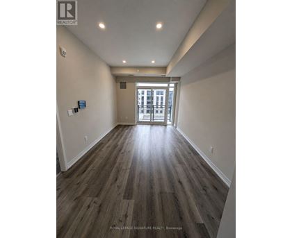 A hallway with wood flooring and white walls leading to a door.
