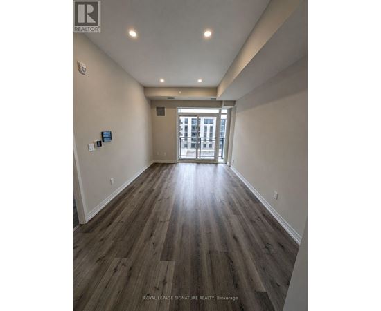 A hallway with wood flooring and white walls leading to a door.