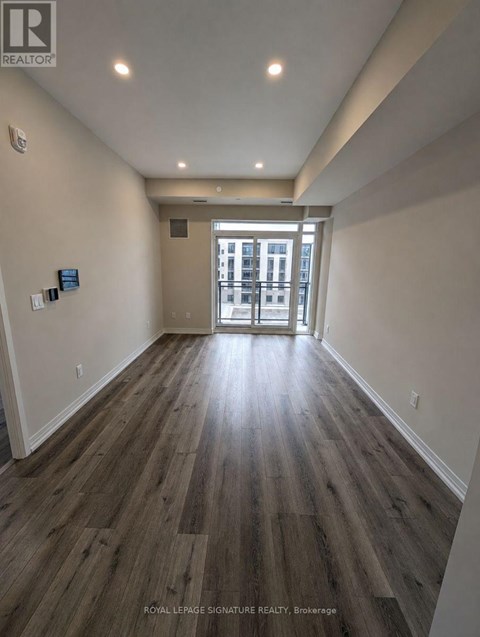 A hallway with wood flooring and white walls leading to a door.