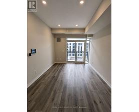 A spacious room with wooden flooring and a view of a building through the glass door.