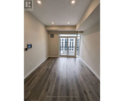 A spacious room with wooden flooring and a view of a building through the glass door.