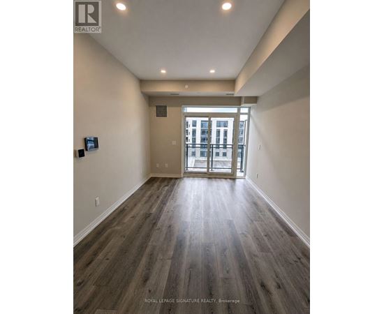A spacious room with wooden flooring and a view of a building through the glass door.