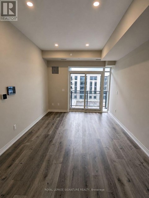 A spacious room with wooden flooring and a view of a building through the glass door.