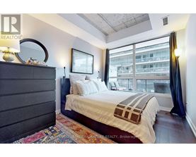A bedroom with a large bed and a view of a building outside the window.