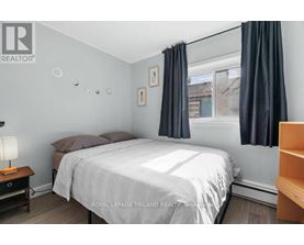 A bedroom with a bed, nightstand, and window with curtains.