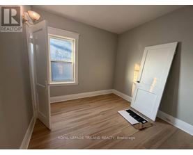 A room with a door open to a hallway, a window, and a wooden floor.