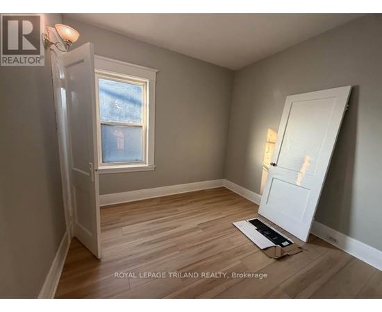 A room with a door open to a hallway, a window, and a wooden floor.