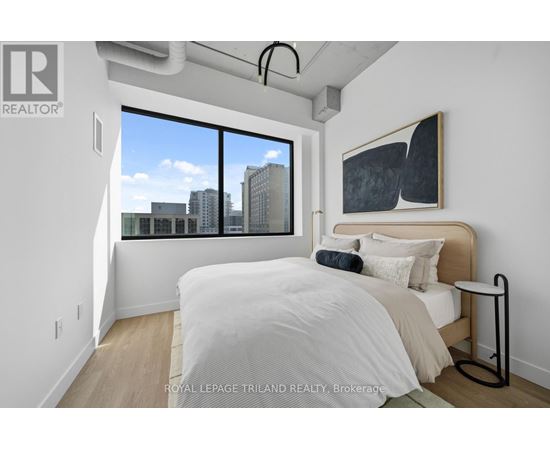 A bedroom with a large bed and a city view through the window.