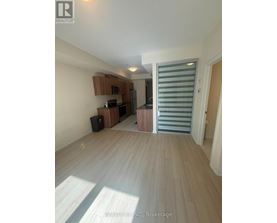 A spacious room with wooden flooring and a kitchen area in the background.