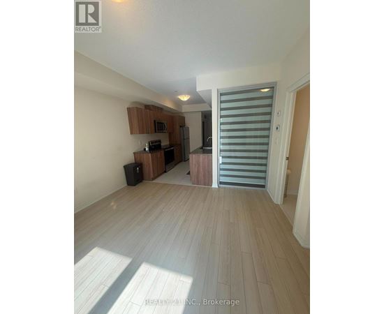 A spacious room with wooden flooring and a kitchen area in the background.